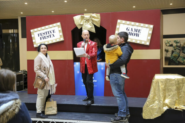 A gameshow host stands with a couple and a baby taking part in a Christmas game show