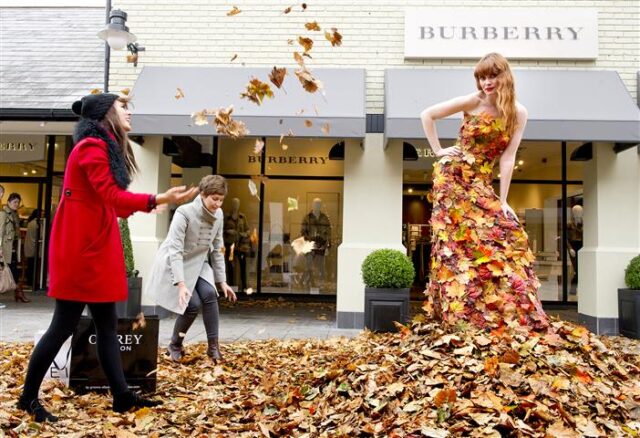 Two shoppers throw autumn leaves at a model in a dress made f leaves