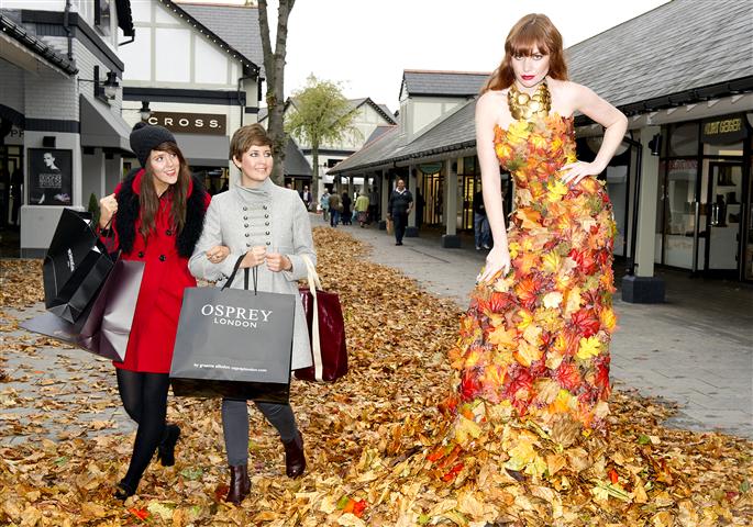 A model in a dress made of autumn leaves next to two shoppers