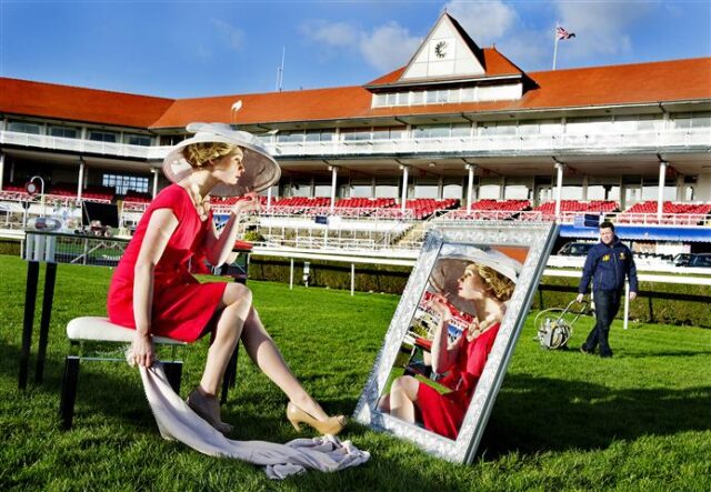 A model looks into a mirror on a racecourse