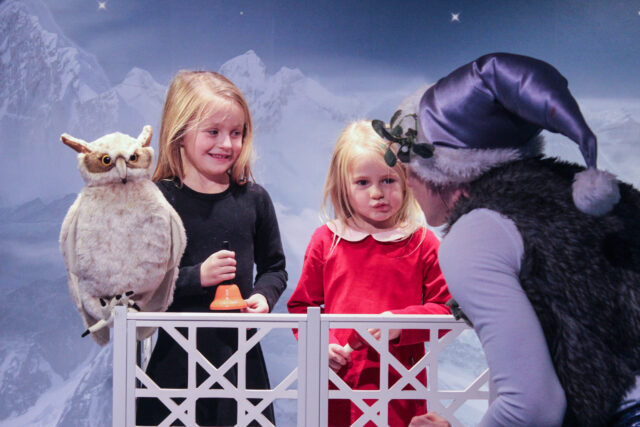 Two children look at the owl character with an elf