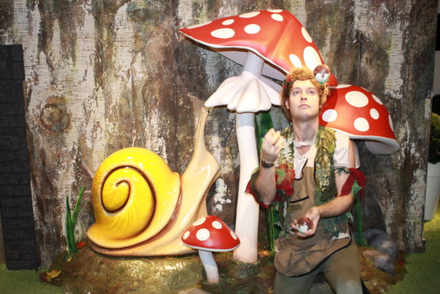 A woodland elf stands in front of a giant toadstool, juggling