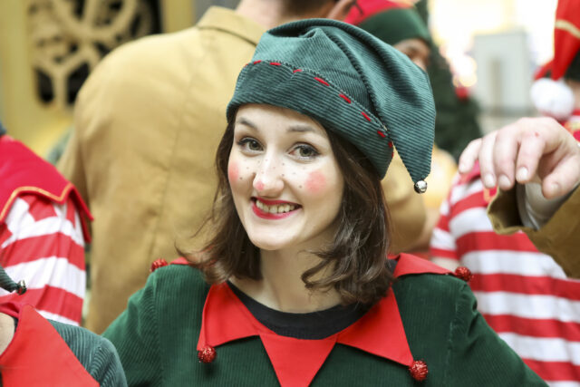 A young lady dressed as a Christmas elf smiles into the camera