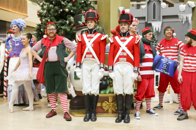 Entertainers dressed as soldiers and elves stand in front of a tree