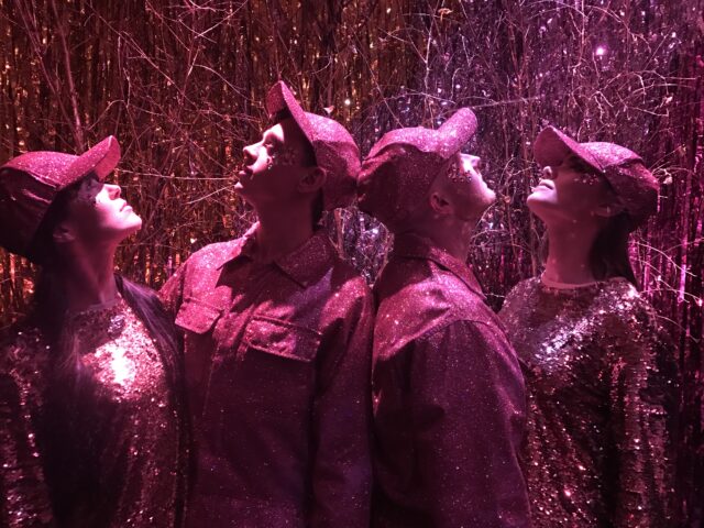 A pink posed photo of four performers